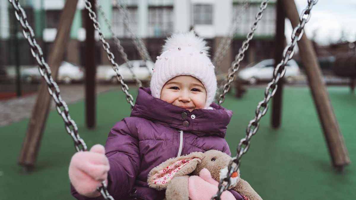 a little girl sitting on a swing with a stuffed animal